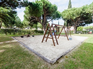 A playground with a swing set and seesaw in a park with trees and grass. - Aldeia das Açoteias Apartment by Interhome (Albufeira)