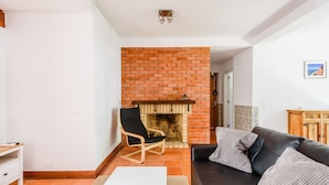 Ein Wohnzimmer mit Kamin aus Backstein, einer schwarzen Ledersofa, einem Holzstuhl und einem weißen Tisch.