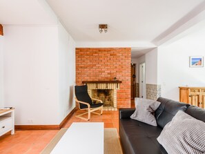 A living room with a brick fireplace, a black leather sofa, a wooden chair, and a white table. - Apartment  by Interhome (Albufeira)