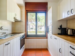 A kitchen with white cabinets, a window, a stove, and a coffee maker. - Apartment  by Interhome (Albufeira)