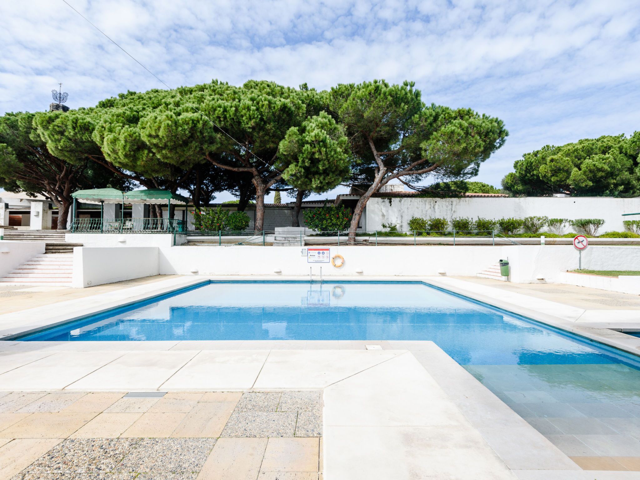 A swimming pool with a lifeguard stand, a no swimming sign, and a large tree in the background.