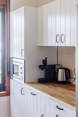 A kitchen with white cabinets, a microwave, a coffee maker, and a kettle on the countertop. - Apartment  by Interhome (Albufeira)