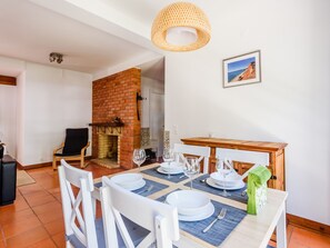 A dining area with a brick fireplace, white chairs, and a table set for four. - Apartment  by Interhome (Albufeira)