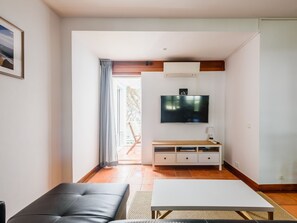 A living room with a sofa, a coffee table, a TV mounted on the wall, and a sliding door leading to an outdoor area. - Apartment  by Interhome (Albufeira)