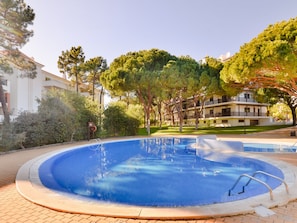 A swimming pool with a clear blue water surface, surrounded by a paved area and trees. - Apartment  by Interhome (Albufeira)