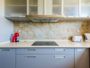 A modern kitchen with a built-in oven, a red kettle, a toaster, and a marble backsplash. - Apartment  by Interhome (Albufeira)