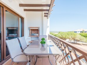 A balcony with a glass table, two chairs, a small potted plant, and a brick fireplace. - Apartment  by Interhome (Albufeira)