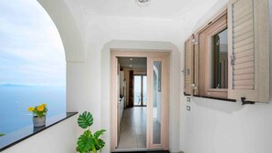 Un balcone con piante in vaso, vista sul mare e una porta che dà su un ambiente interno.