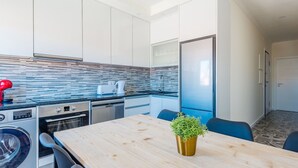 A modern kitchen with a wooden table, a washing machine, a dishwasher, and a refrigerator. - Apartment  by Interhome (Lisbon)