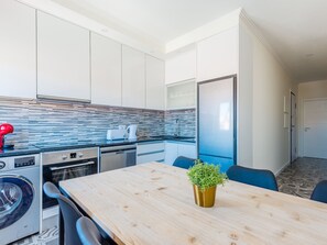 A modern kitchen with a wooden table, a washing machine, a dishwasher, and a refrigerator. - Apartment  by Interhome (Lisbon)