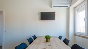 A conference room with a long wooden table, six chairs, a potted plant, a flat-screen TV mounted on the wall, and an air conditioning unit. - Apartment  by Interhome (Lisbon)