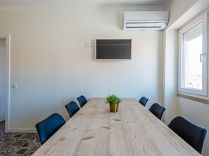 A conference room with a long wooden table, six chairs, a potted plant, a flat-screen TV mounted on the wall, and an air conditioning unit. - Apartment  by Interhome (Lisbon)
