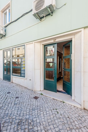 A building with a cobblestone street entrance, numbered 87, and a green door with a window. - Apartment  by Interhome (Lisbon)