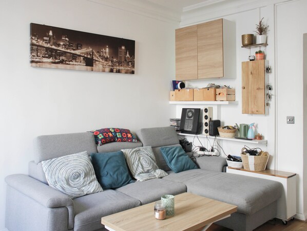 A modern living room with a grey sofa, a coffee table, and a cityscape painting on the wall. - 2-bedroom apartment - Eiffel Tower (Paris)