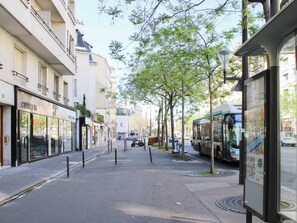 Eine Stadtstraße mit Gebäuden, einer Bushaltestelle und einem baumgesäumten Bürgersteig.