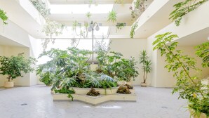 Um amplo átrio com vários níveis de vegetação, incluindo plantas em vasos grandes e plantas pendentes, e um chão com padrão.