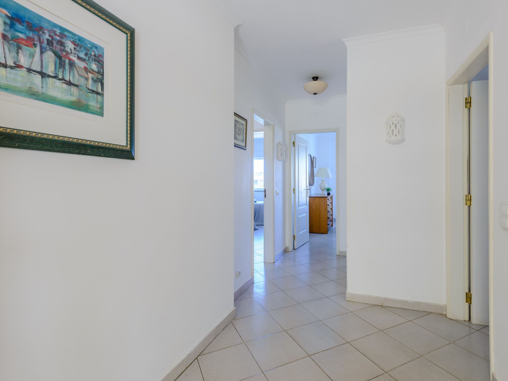 A hallway with a tiled floor, a door on the right, and a painting on the left.