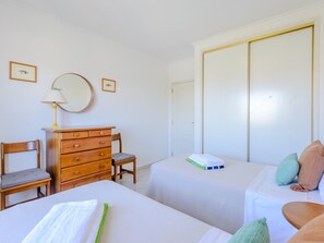A hotel room with two beds, a wooden dresser, a chair, a mirror, and a wardrobe. - Apartment  by Interhome (Vilamoura)