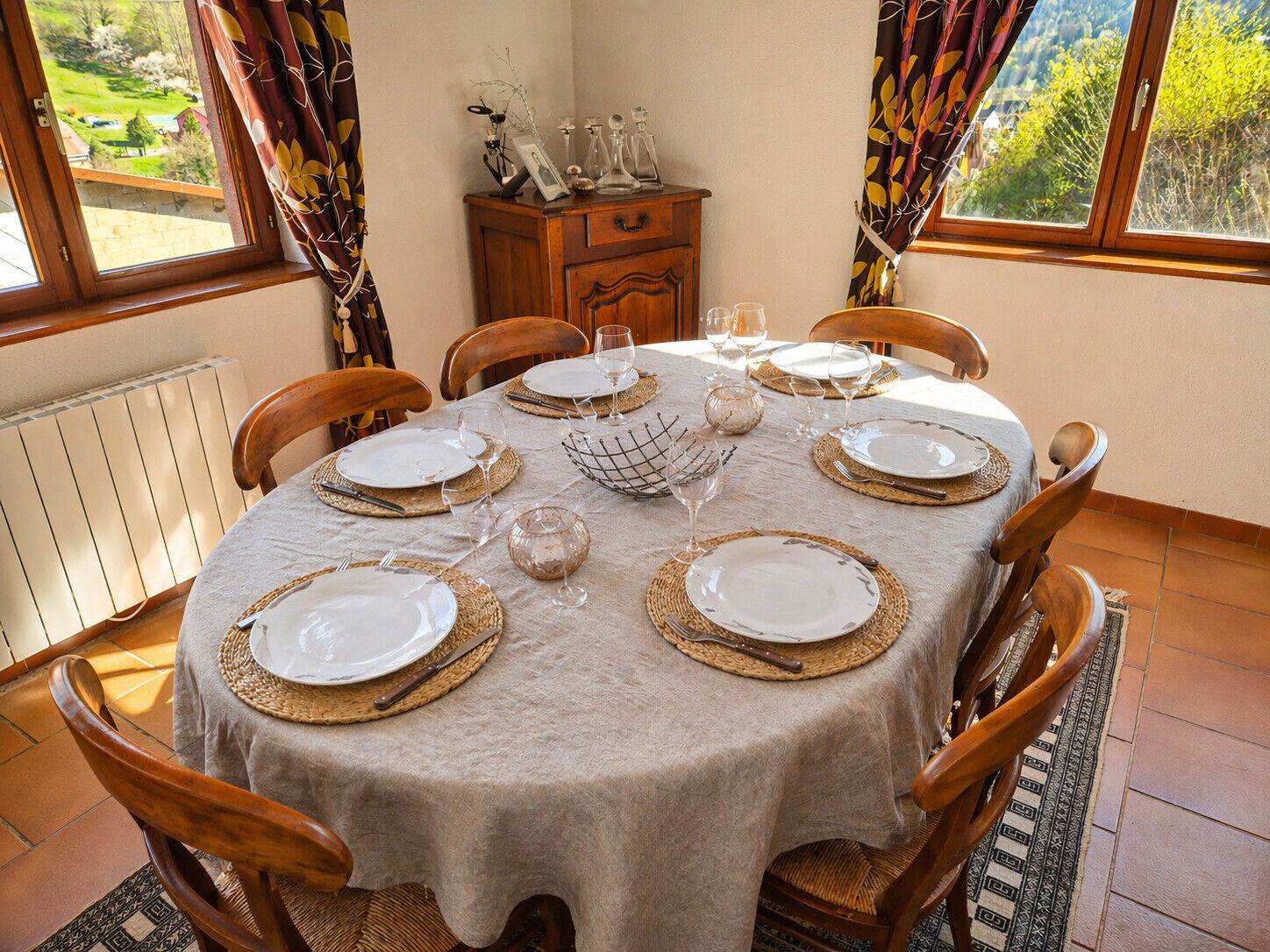 A dining table set for six with plates, cutlery, and glasses, surrounded by wooden chairs.