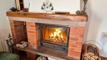 A brick fireplace with a fire, a mantel shelf with decorative items, and a green upholstered bench.