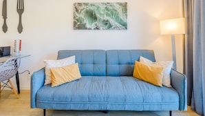 A blue sofa with two pillows, a wall-mounted picture, a table with a lamp, and a chair. - Apartment  by Interhome (Carvoeiro (Algarve))