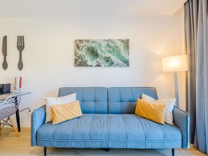 A blue sofa with two pillows, a wall-mounted picture, a table with a lamp, and a chair. - Apartment  by Interhome (Carvoeiro (Algarve))