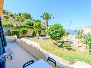 A terrace with a table and chairs, overlooking a landscaped garden with various plants and a view of the sea. - Apartment  by Interhome (Carvoeiro (Algarve))
