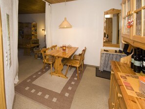 A dining area with a wooden table and chairs, a hanging light fixture, and a kitchen area with a wooden cabinet and wine bottles. - Wohnung Lippmeyer, (Splügen), by Interhome (Splügen)