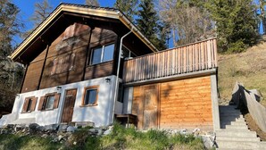 A wooden chalet with a balcony, stone foundation, and a staircase leading up.