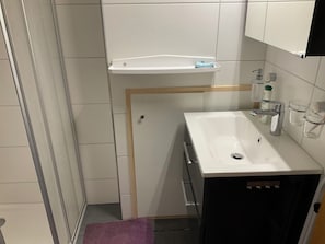 Ett badrum med ett vitt handfat, en spegel, en handdukshängare och en duschhörna.