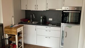 A compact kitchen with white cabinets, a stainless steel sink, a black countertop, and a built-in oven.