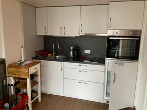 A compact kitchen with white cabinets, a black countertop, a stainless steel oven, and a small refrigerator.