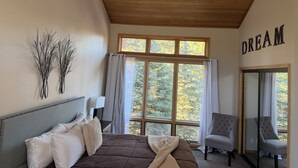 Un dormitorio con una cama, dos sillas, un ventanal con cortinas y una pared con la palabra 'DREAM' escrita encima.