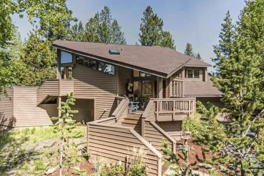 A two-story cabin with a deck, surrounded by trees.