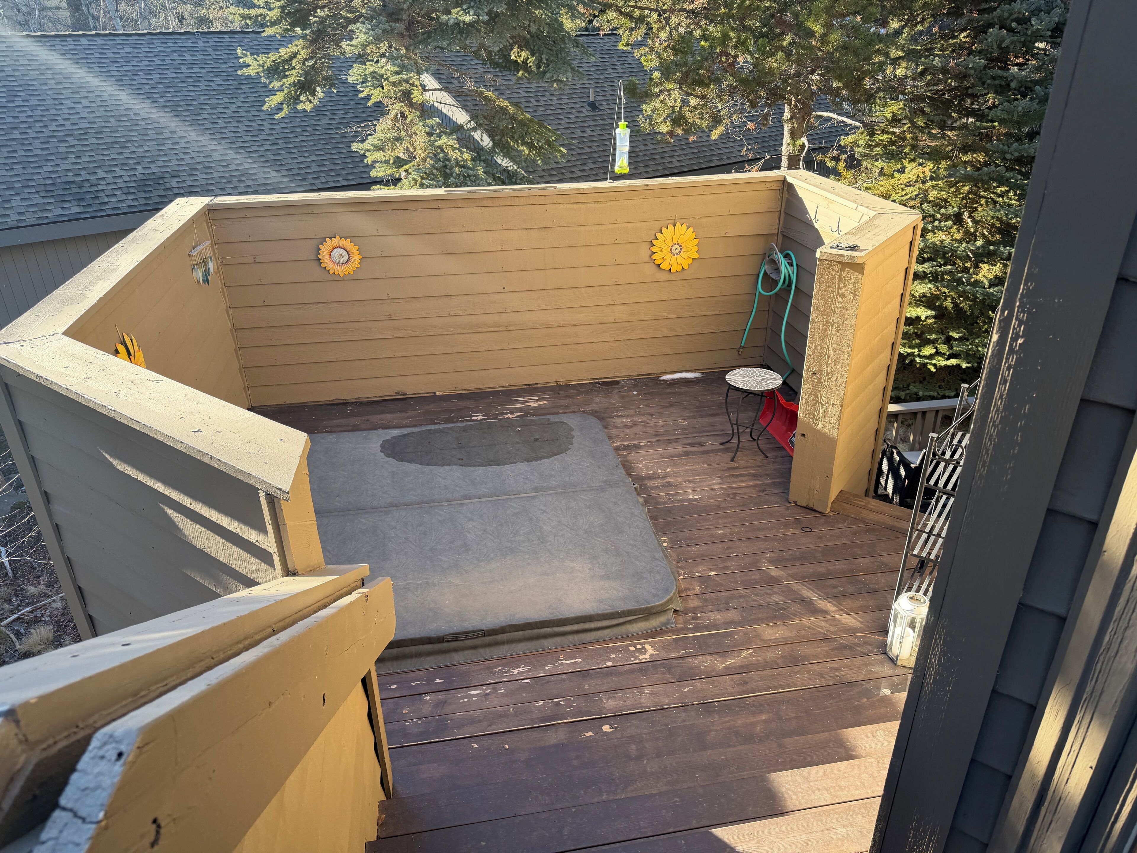 A wooden deck with a hot tub, two flower decorations, and a hose.