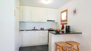 A kitchen with white cabinets, a black tiled floor, and two wooden stools.