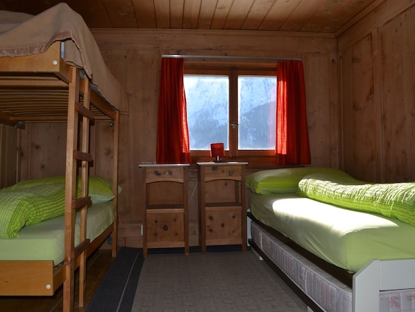 Una habitación de cabaña de madera con literas, un escritorio y una ventana con cortinas.