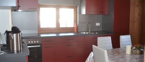 A compact kitchen with red cabinets, a stainless steel stove, and a dining table with a festive tablecloth.