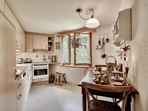 A kitchen with wooden cabinets, a stove, a dining table with chairs, and a window with curtains.