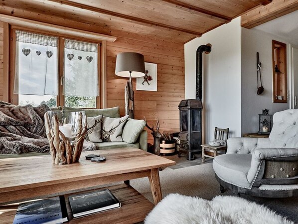 A cozy cabin interior with a sofa, a table with books, a lamp, and a fireplace.