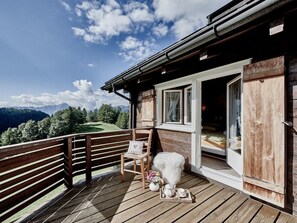 A wooden deck with a chair and a small table, overlooking a mountainous landscape.