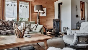 Una habitación acogedora con techo de madera, un sofá, una mesa con libros, una lámpara y una chimenea.