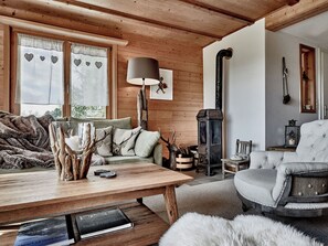 A cozy room with a wooden ceiling, a sofa, a table with books, a lamp, and a fireplace. - Chalet Lieuretta da Tscharfs, (Feldis). by Interhome (Tomils)