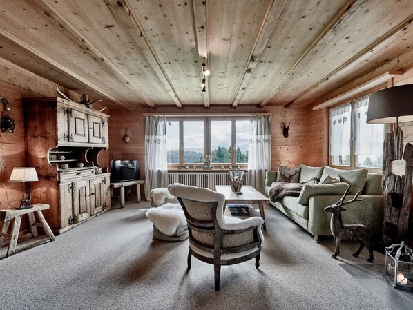A cozy cabin interior with a wooden ceiling, a dining table, a sofa, and a television.