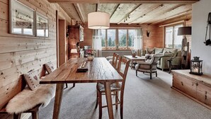 Interior de una cabaña de madera con una mesa de comedor, sillas, un sofá y una chimenea.