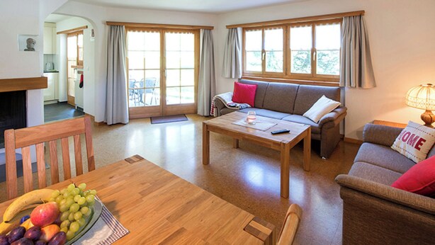 Ein geräumiges Wohnzimmer mit einer Couch, einem Esstisch mit Obst und großen Fenstern.