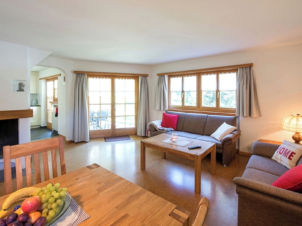 A spacious living room with a sofa, a dining table with fruit, and large windows. - Ferienhaus Muntschi, (Andeer), by Interhome (Andeer)