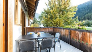 Eine Terrasse im Freien mit Tisch und Stühlen, einem Holzzaun und Blick auf Bäume und Hügel.