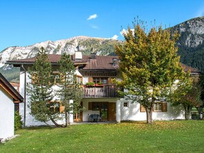 A two-story building with a balcony, surrounded by a grassy area and a mountain backdrop. - Ferienhaus Muntschi, (Andeer), by Interhome (Andeer)