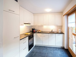 A compact kitchen with white cabinets, a stove, a sink, and a window with a view. - Ferienhaus Muntschi, (Andeer), by Interhome (Andeer)